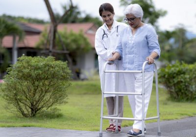 Indian woman nursing home worker caring for elderly woman walking with walking aid, nursing care.
