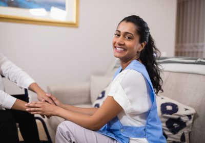Portrait of smiling young doctor touching patient hands at home